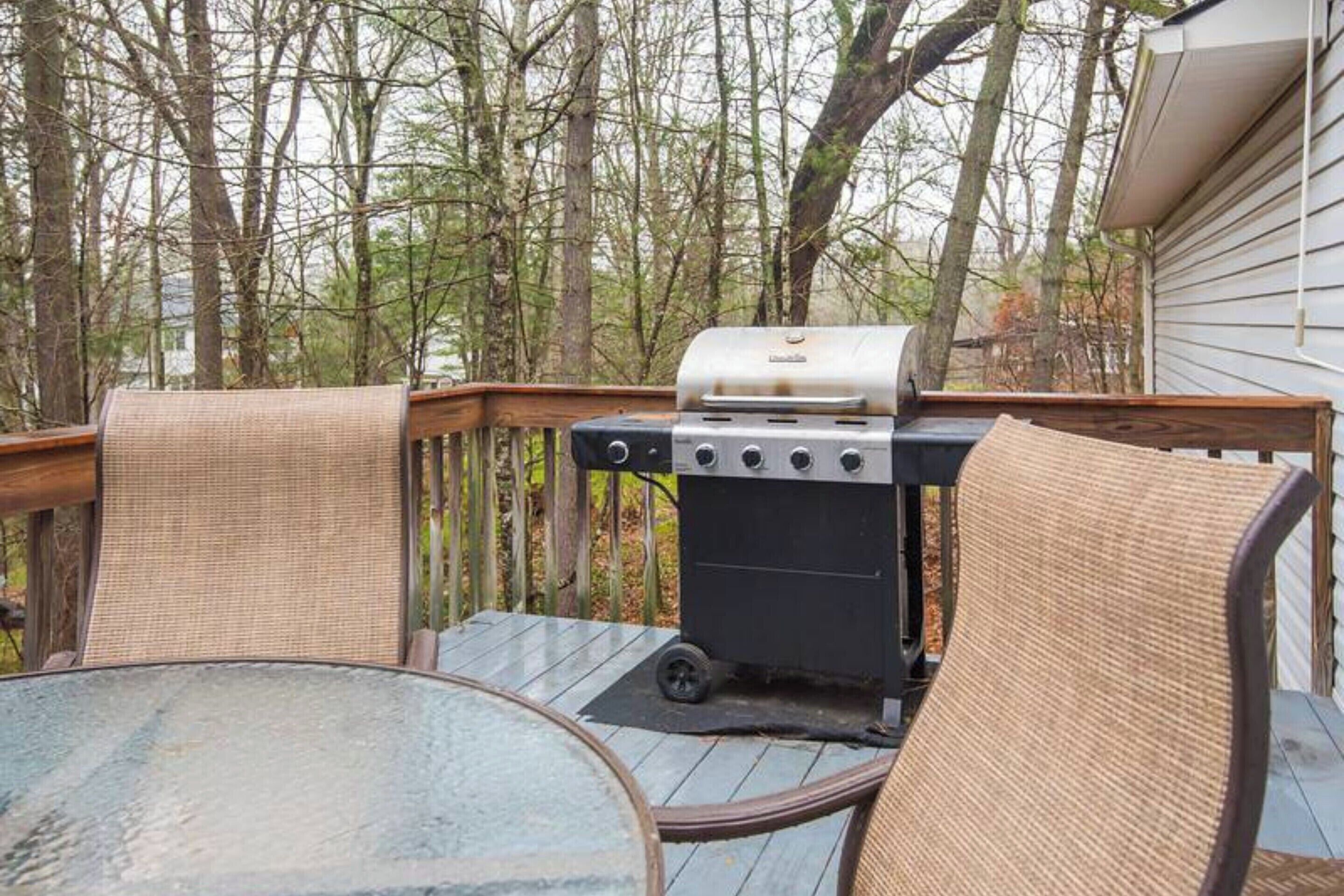 Una terraza con una parrilla, sillas de mimbre y una mesa de vidrio.