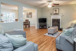 A living room with a fireplace, a television, and a ceiling fan.