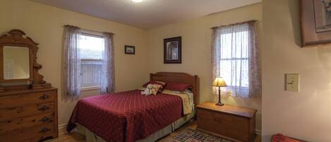 A bedroom with a wooden bed, a dresser, a nightstand with a lamp, and a window with curtains.