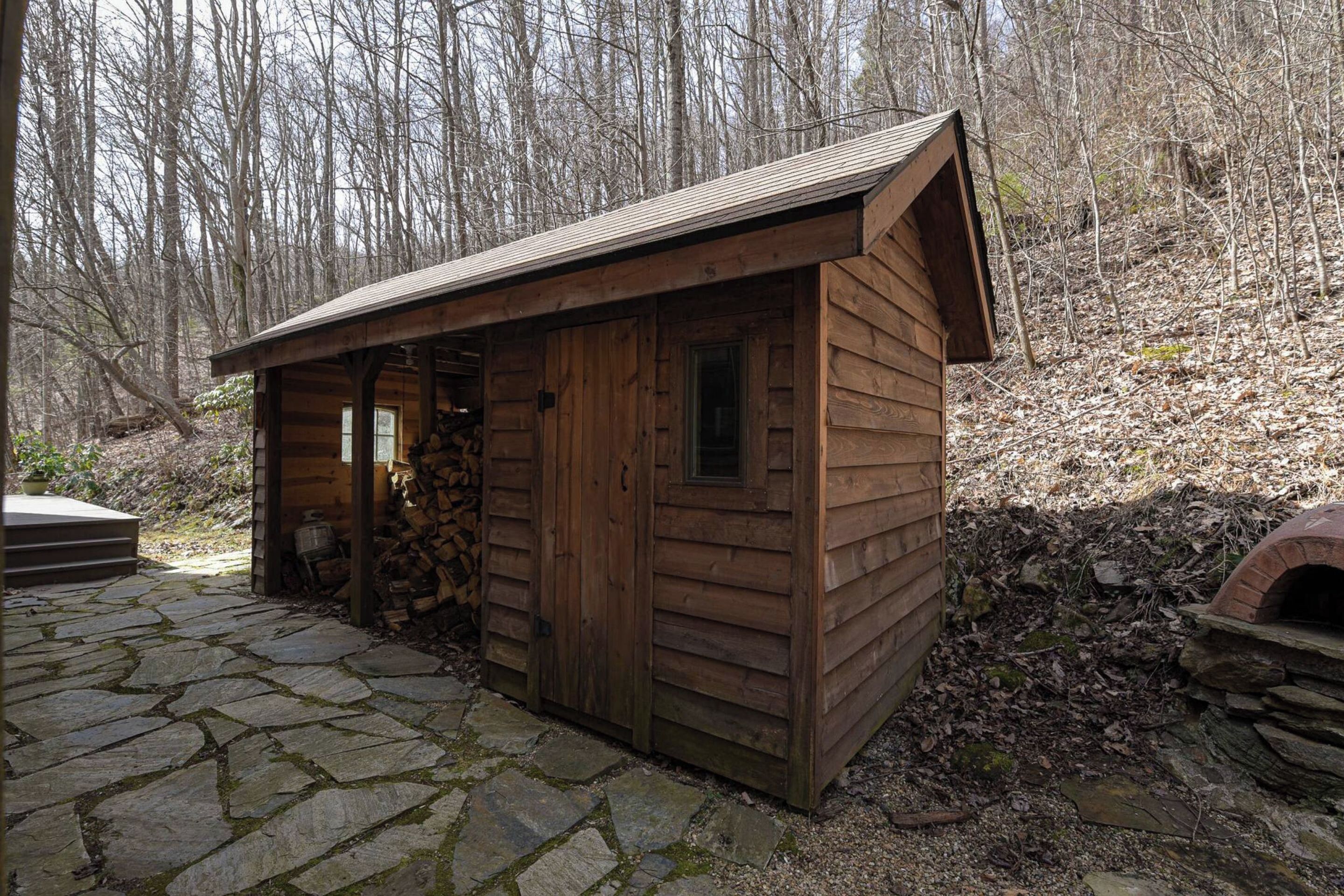 Una cabaña de madera con entrada empedrada de piedra, un ventanal pequeño y una chimenea.