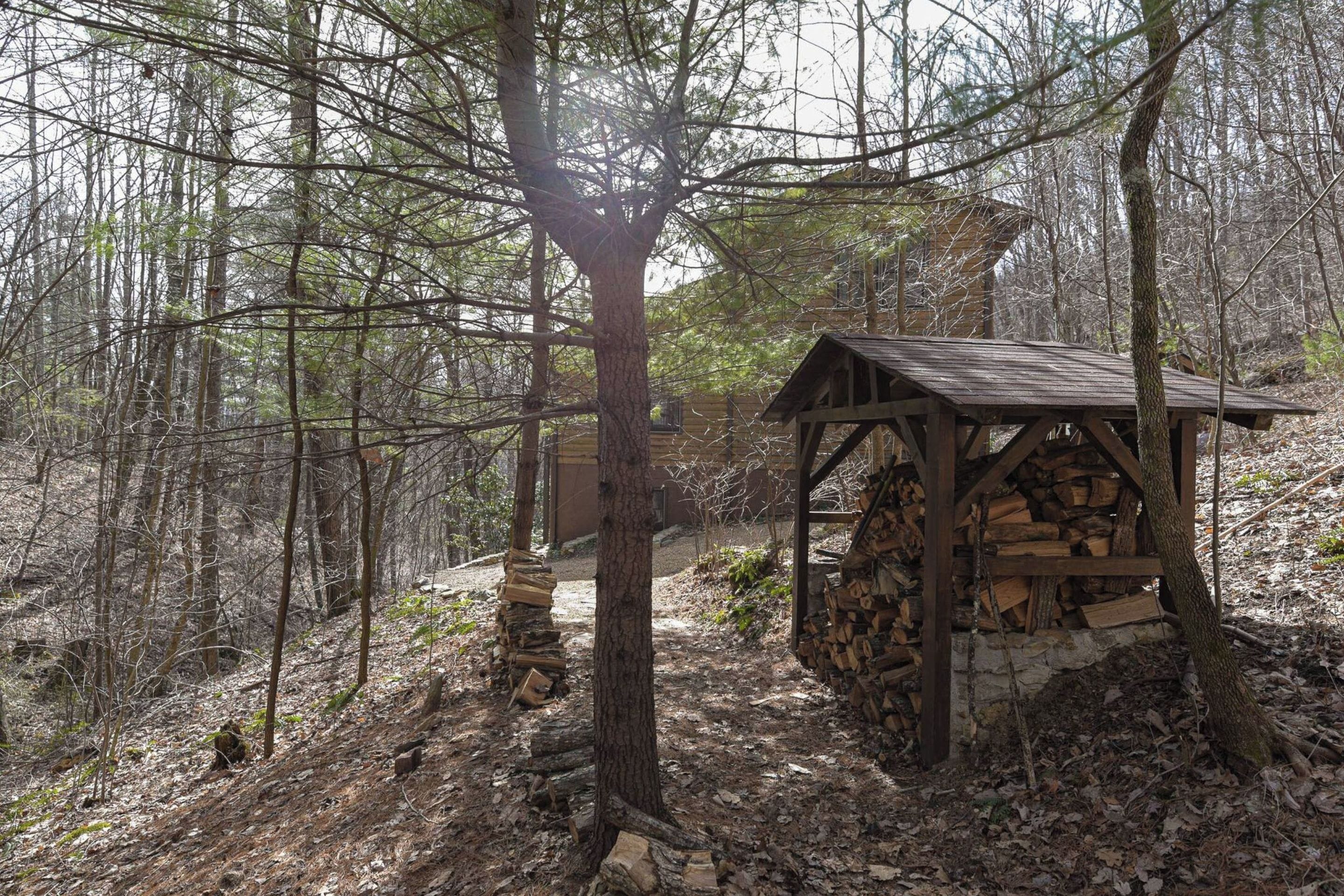 A rustic wooden structure in a forested area with a pile of firewood.