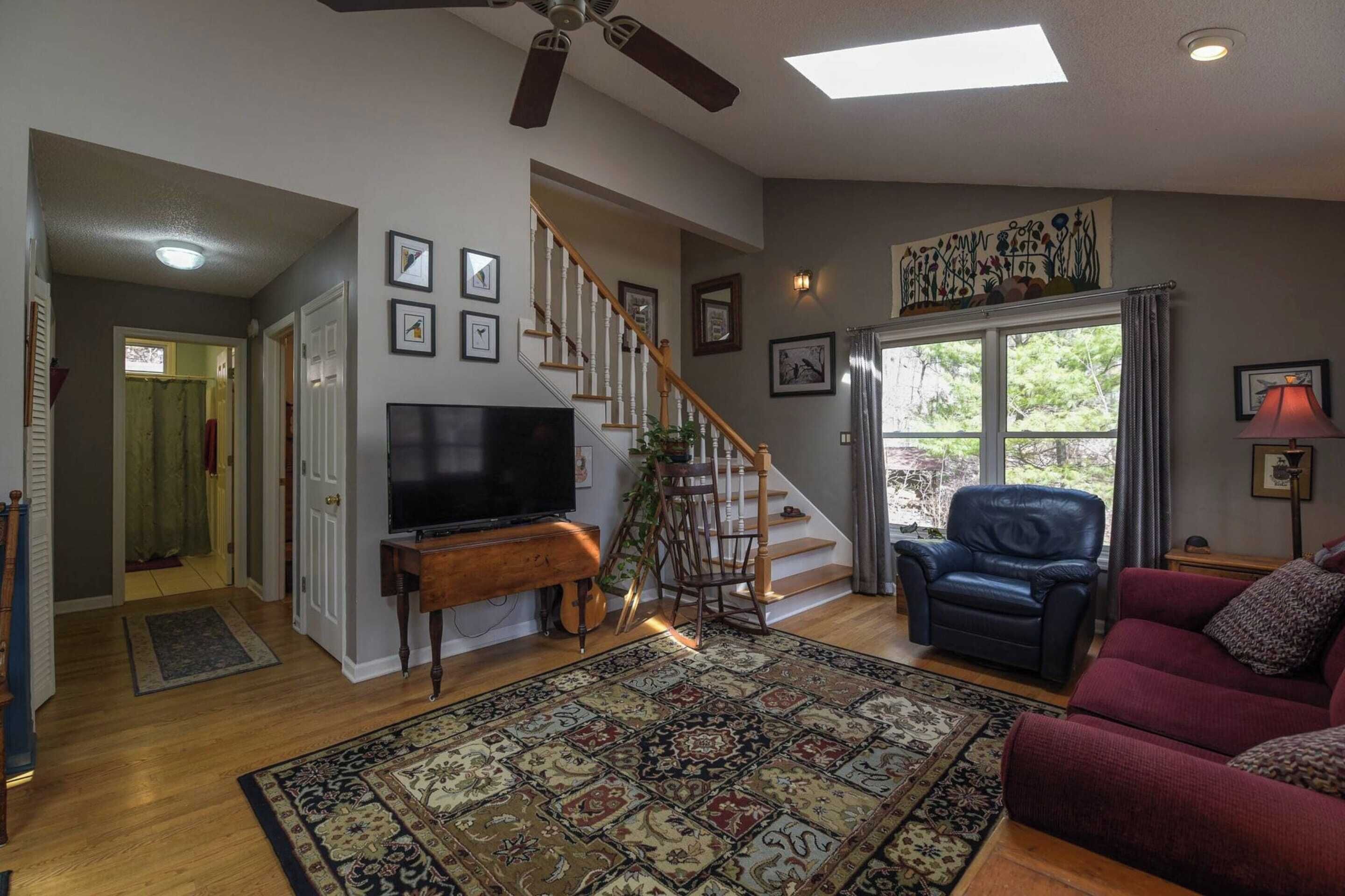 A living room with a wooden staircase, a flat-screen TV, a red sofa, and a patterned rug.