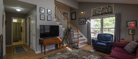 A living room with a wooden staircase, a flat-screen TV, a red sofa, and a patterned rug.