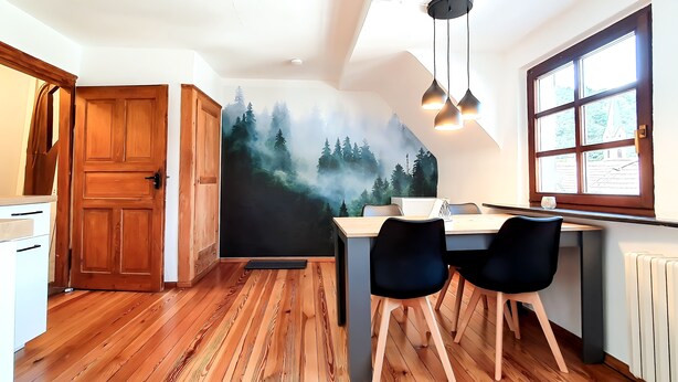 Una cucina con mobili in legno, un tavolo da pranzo con sedie, un'ampia finestra con tende e un murale raffigurante una foresta.