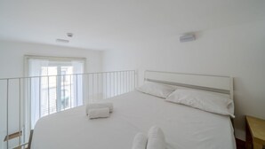 Quarto com cama grande, janela com vista, varanda e decoração em tons de branco.