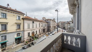 Vista da rua com edifícios, uma varanda e carros na via.