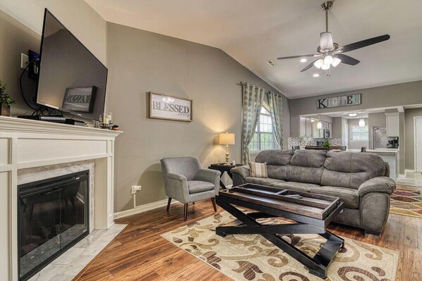 A living room with a fireplace, a television, a sofa, and a ceiling fan.