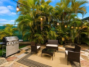 An outdoor patio with a grill, wicker furniture, and string lights.