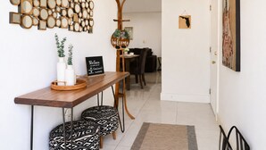 A modern interior with a wooden reception desk, patterned ottomans, a wall-mounted mirror collage, a welcome sign, and a guitar. - Acogedora Casa con Excelente Ubicacion (Miami)