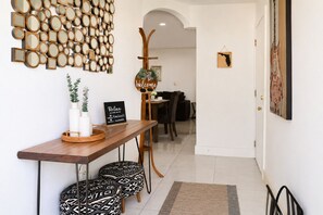 A modern interior with a wooden reception desk, patterned ottomans, a wall-mounted mirror collage, a welcome sign, and a guitar.
