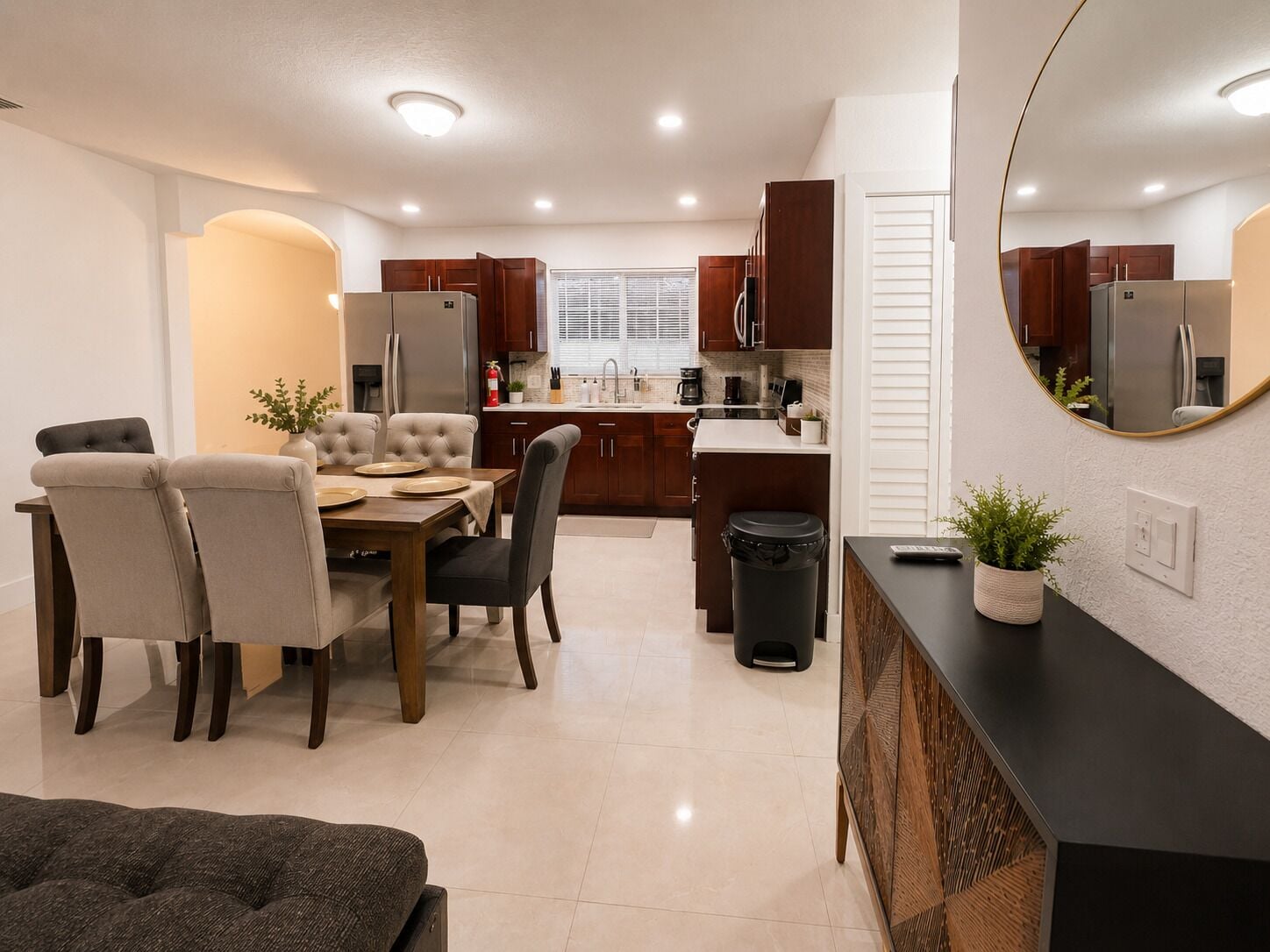 Una cucina moderna con pensili in legno scuro, un'area pranzo con tavolo e sedie, e un cestino nero.