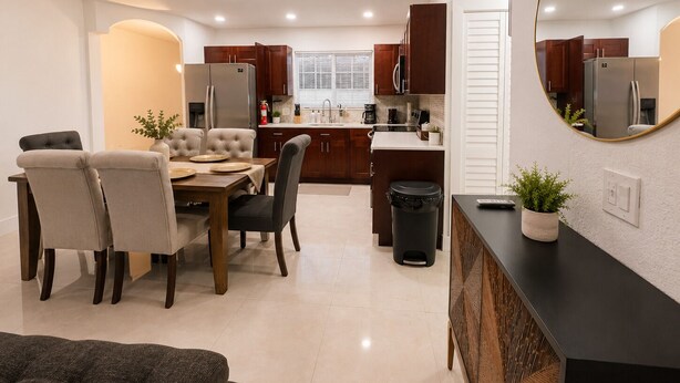 A modern kitchen with dark wooden cabinets, a dining area with a table and chairs, and a black trash bin. - Acogedora Casa con Excelente Ubicacion (Miami)