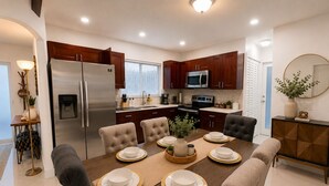 A modern kitchen with dark wood cabinets, stainless steel appliances, and a dining area with a wooden table set for four. - Acogedora Casa con Excelente Ubicacion (Miami)