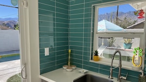 A kitchen with teal tiles, a stainless steel sink, and a window with a view of mountains. - Amarillo  (Palm Springs)