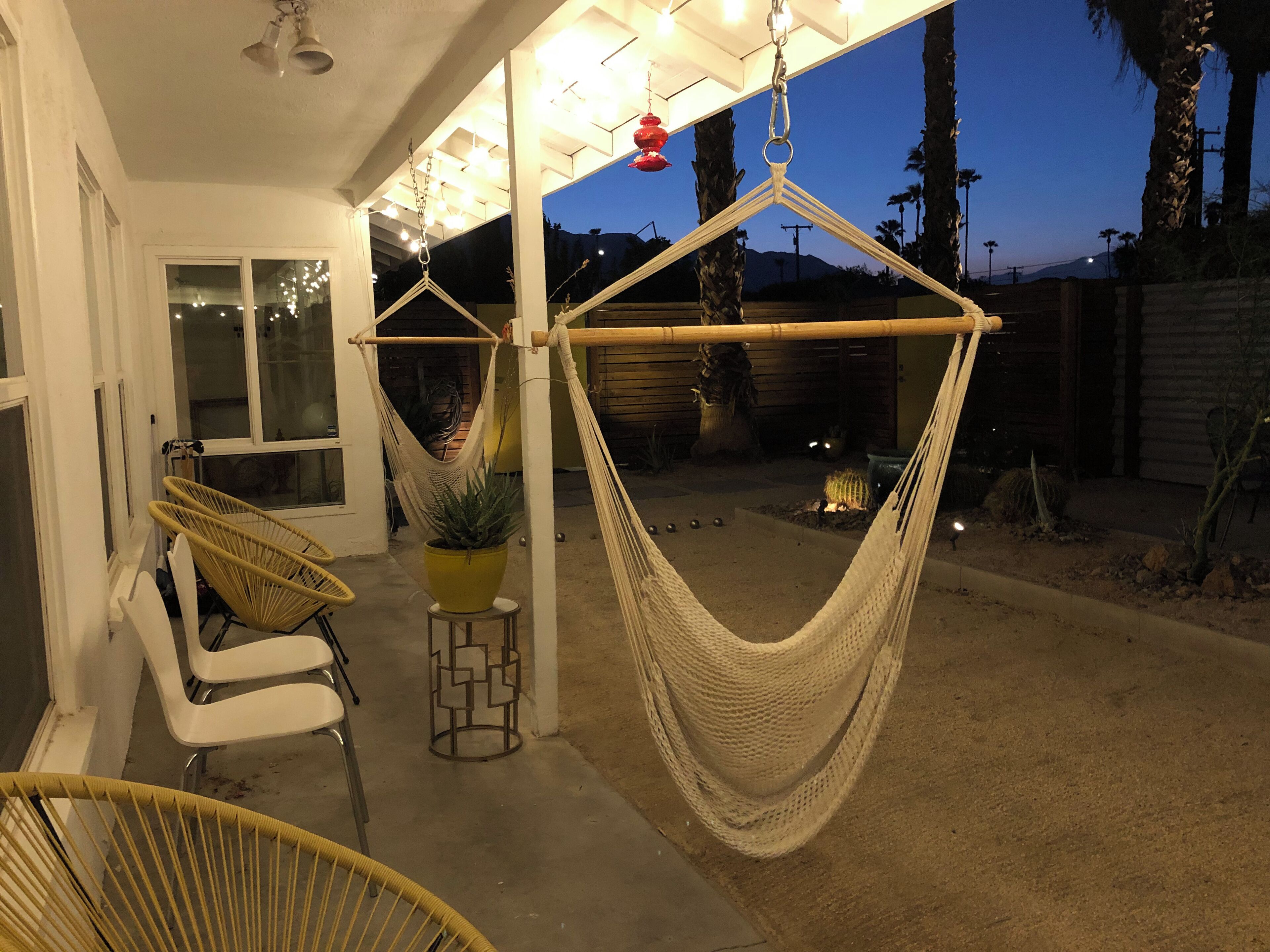 A hammock chair, a yellow potted plant, and a white chair under a covered patio area.