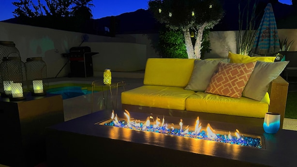 A modern outdoor seating area with a yellow sofa, a fire feature, and decorative lanterns. - Amarillo  (Palm Springs)