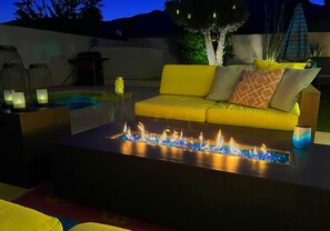 A modern outdoor seating area with a yellow sofa, a fire feature, and decorative lanterns. - Amarillo  (Palm Springs)