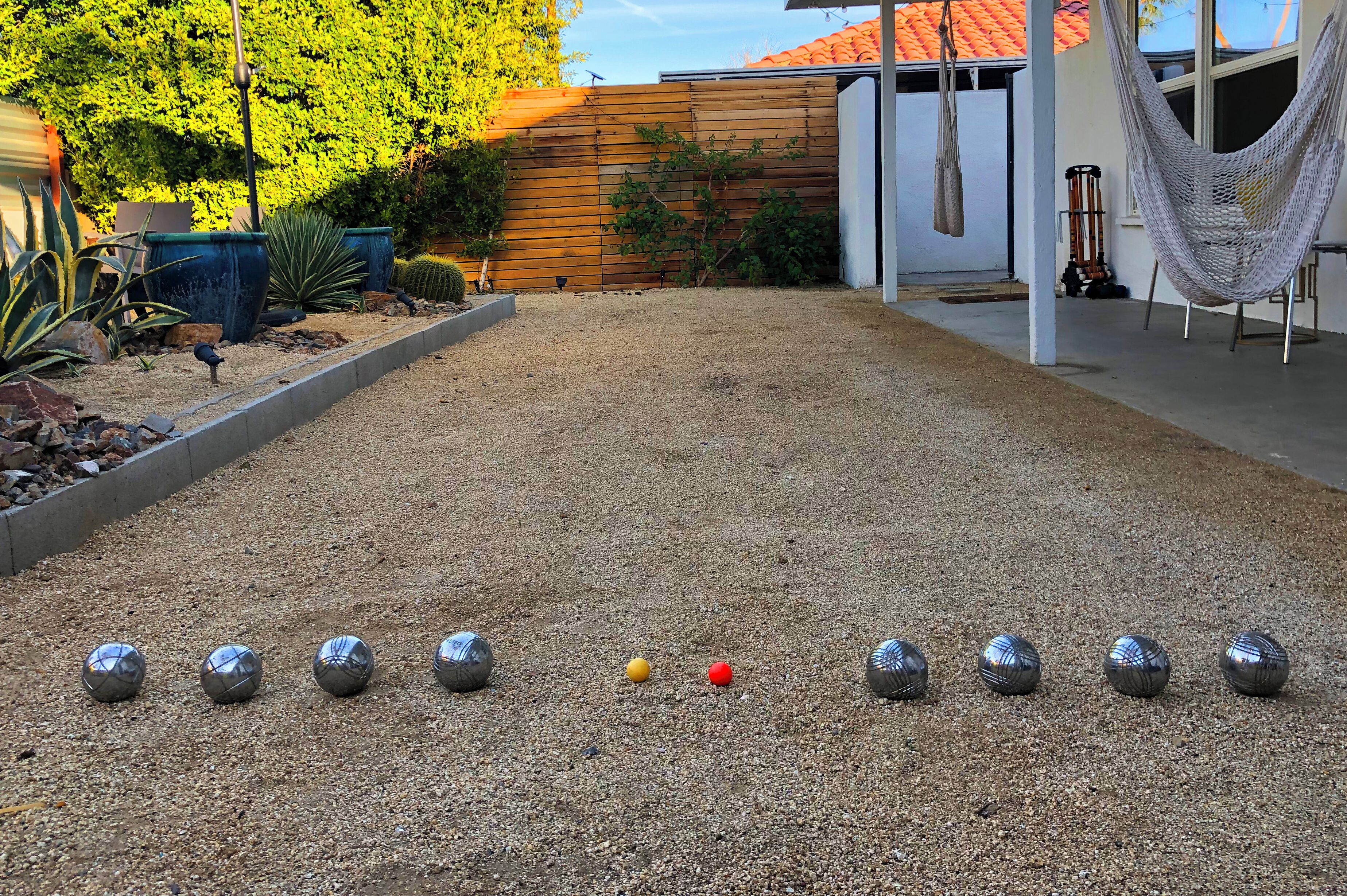 A courtyard with a gravel surface, a wooden fence, and a hammock.