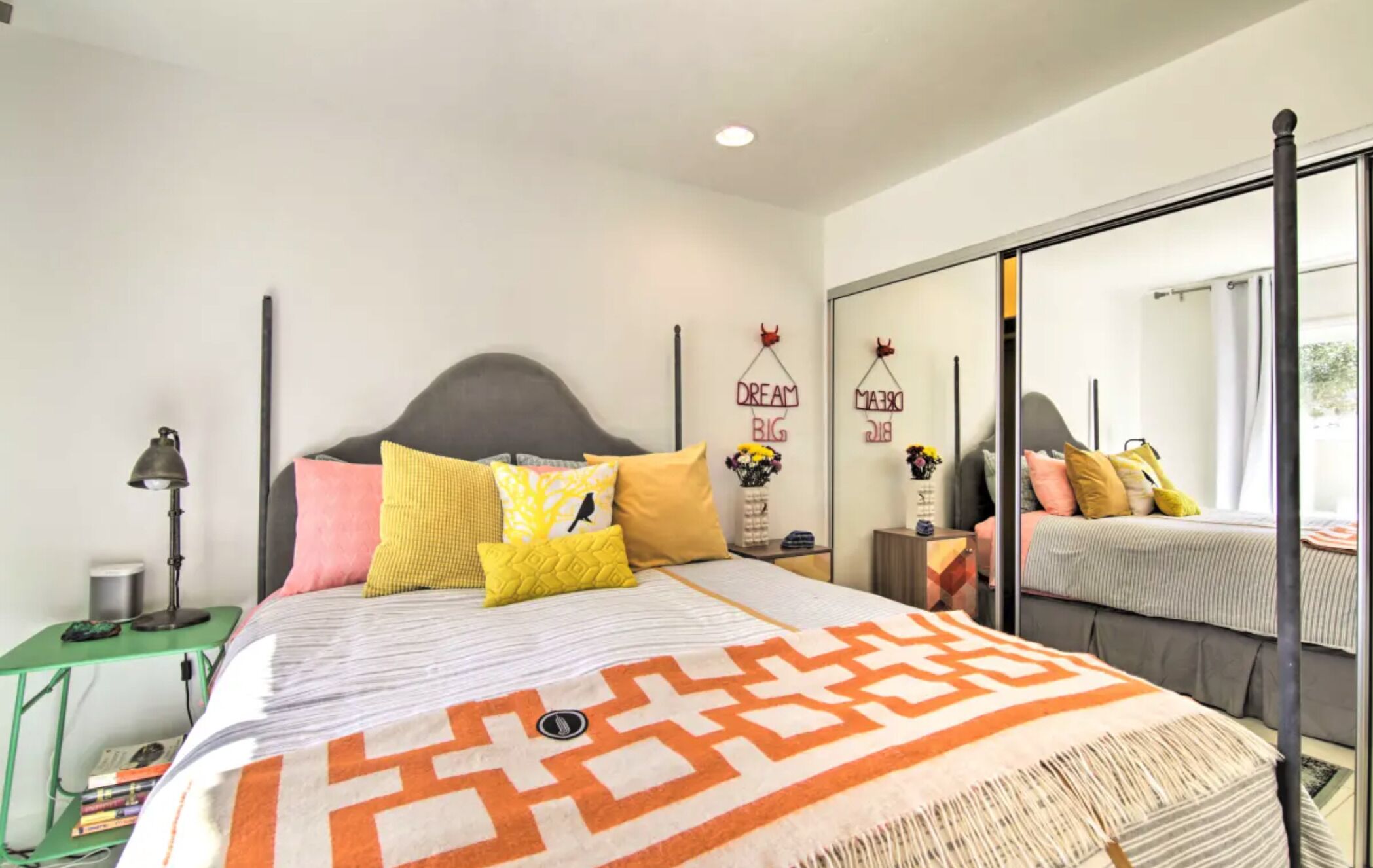 A bedroom with a bed, bedside table, lamp, and a mirror.