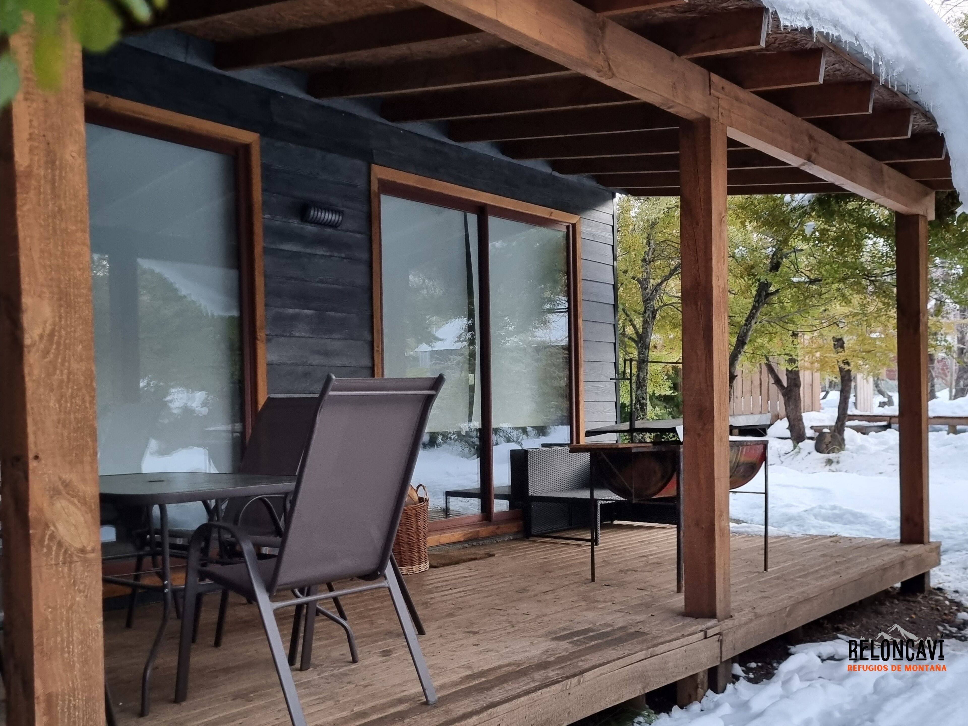 Un patio techado al aire libre con mesa y sillas, una terraza de madera y vistas a un paisaje nevado.