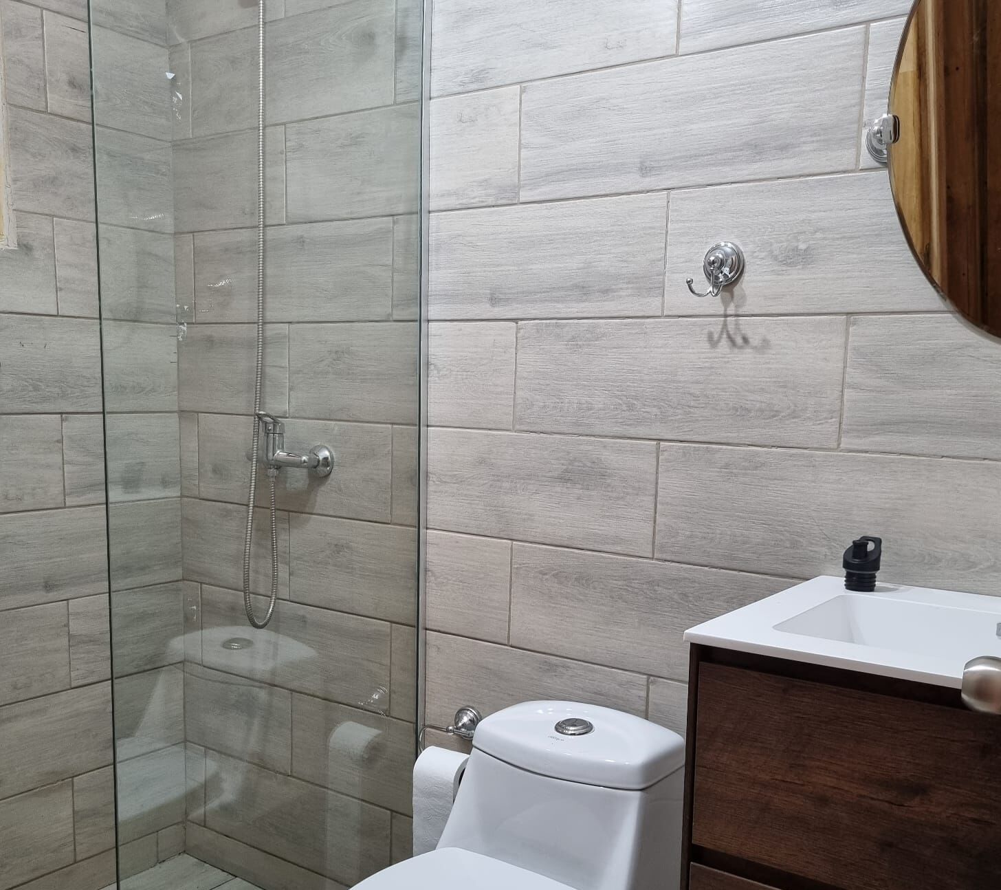 Un baño con ducha envuelta en vidrio, inodoro blanco y tocador de madera con lavamanos.