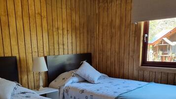 Una stanza con due letti, rivestimenti in legno sulle pareti, una finestra con vista su un edificio esterno e una lampada sul comodino.
