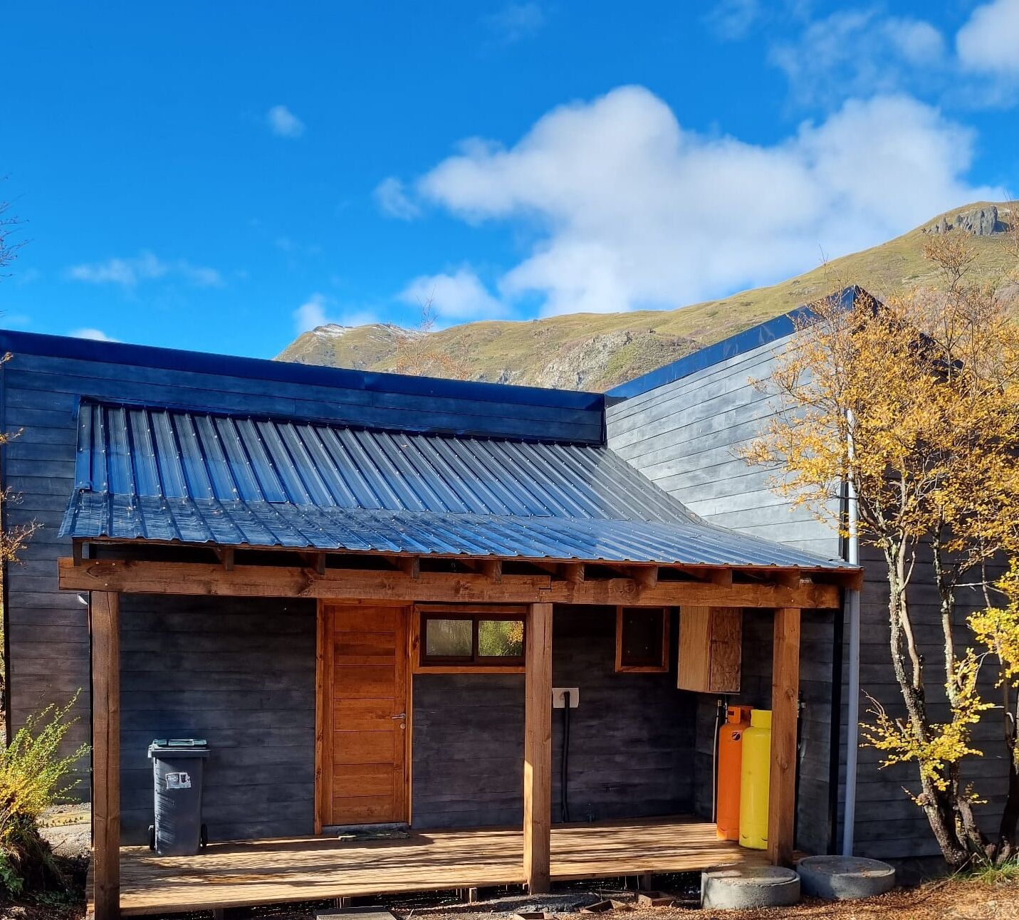 Une cabane rustique avec un toit en métal à pente, des murs en bois et un porche à l’avant.