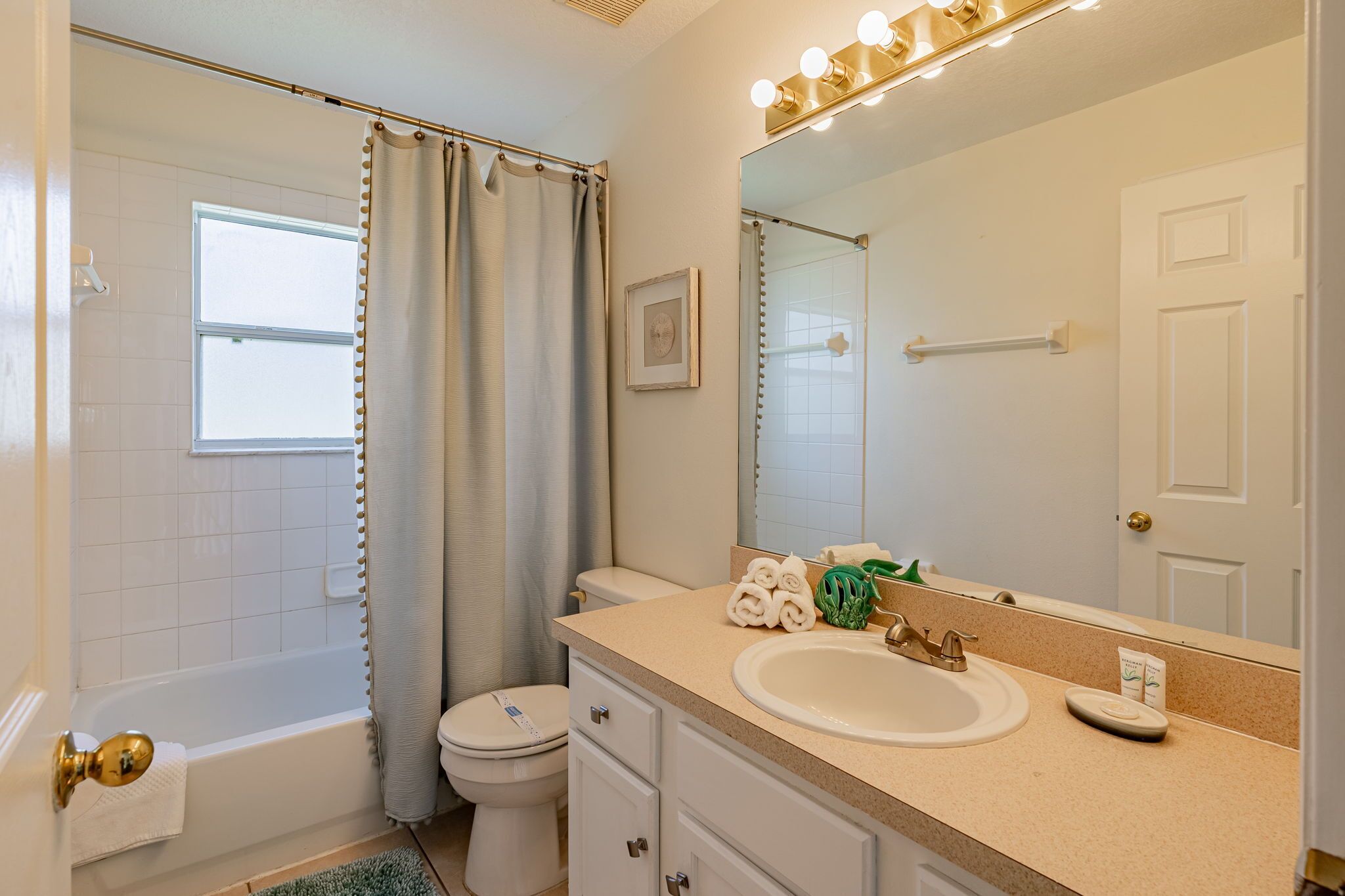 A bathroom with a bathtub, toilet, sink, and a large mirror with lights.