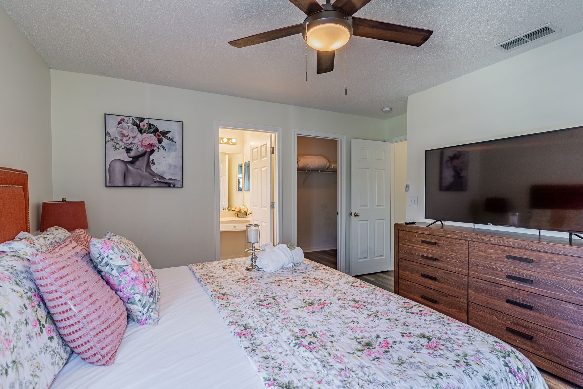 A bedroom with a bed, a ceiling fan, a TV, and a closet.