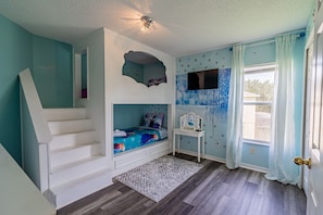 Quarto com cama embutida, uma mesinha, janela com cortinas e uma escada.