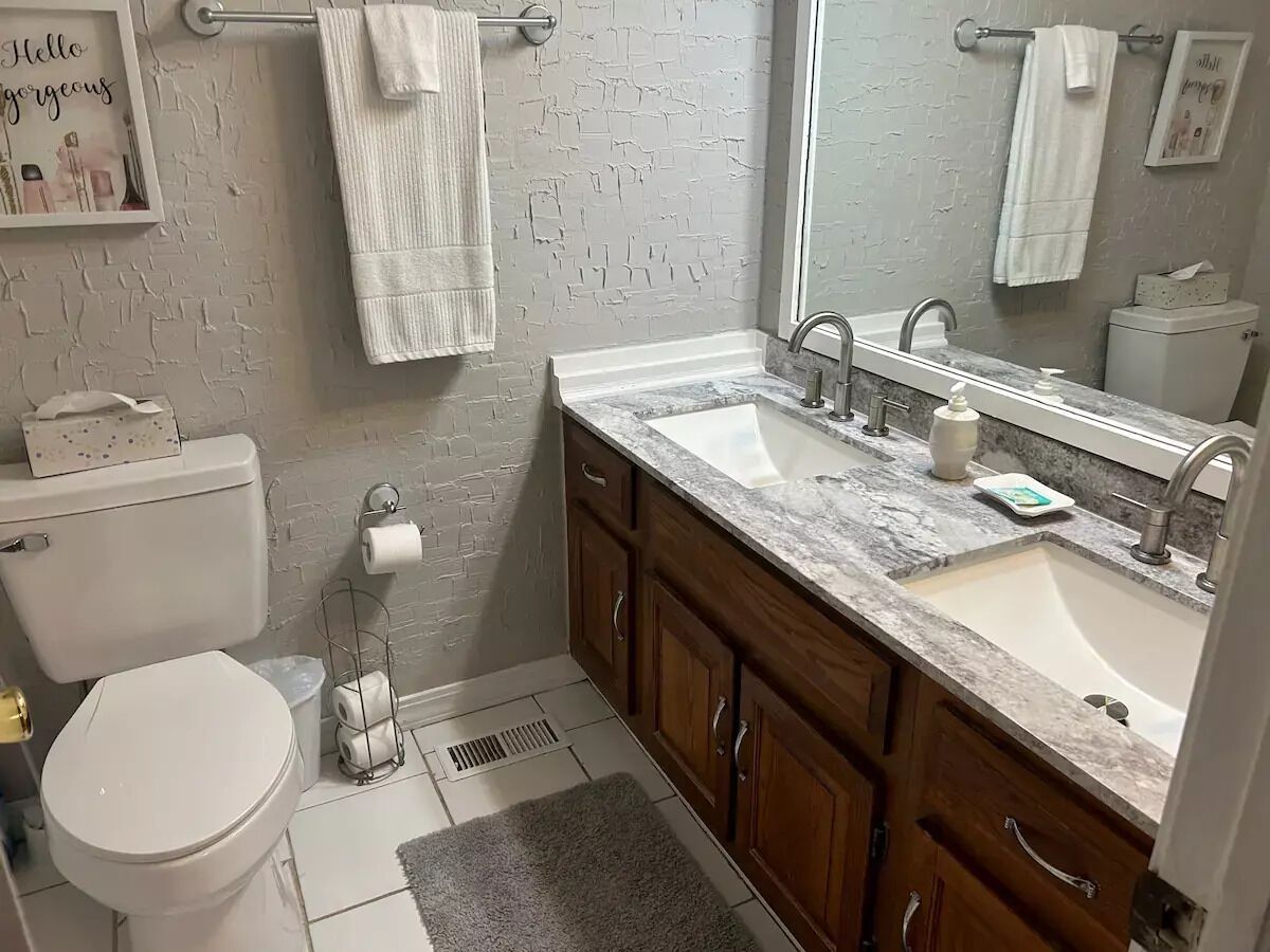 A bathroom with a white toilet, a sink with a marble countertop, wooden cabinets, and a large mirror.