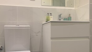 Une salle de bain moderne équipée de toilettes, d’un lavabo avec un miroir et de produits de toilette posés sur le comptoir.