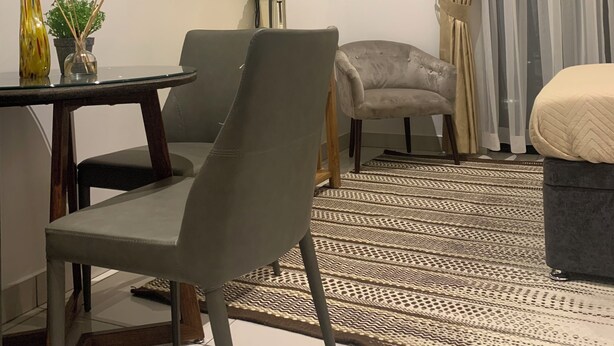 Un salon moderne comprenant un coin repas, un téléviseur à écran plat fixé au mur, un canapé gris, un tapis à motifs et une petite table agrémentée d’objets décoratifs.