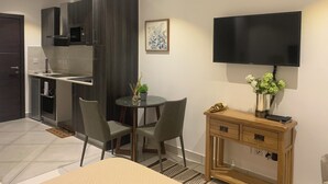 Une cuisine moderne avec des meubles de couleur sombre, un coin repas avec une table ronde et des chaises, et un téléviseur à écran plat fixé au mur.