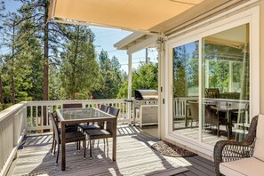 Une terrasse couverte avec une table et des chaises, un barbecue et une porte vitrée donnant sur un espace extérieur.