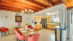 Cocina moderna con armarios de madera, un refrigerador de acero inoxidable y una zona de comedor con mesa de madera y sillas rojas.