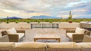 Un patio exterior con mobiliario de mimbre, piscina y montañas al fondo.