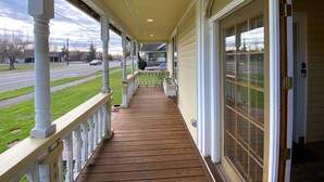 A covered porch with a wooden deck, white railings, and a glass door on the right. - Cozy Cole St Home built in 1910 in Downtown Enumclaw (Enumclaw)