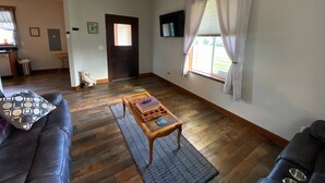 A living room with a dark brown wooden floor, a black leather sofa, a wooden coffee table, and a dog. - Cozy Cole St Home built in 1910 in Downtown Enumclaw (Enumclaw)