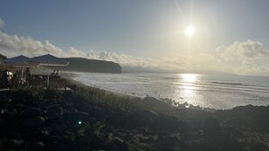 Een strand met een rotsachtige voorgrond, een heldere lucht en een zonnig uitziende zee.