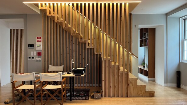 Een modern interieur met een wand van houten latten, een bureau met stoelen en een trap.