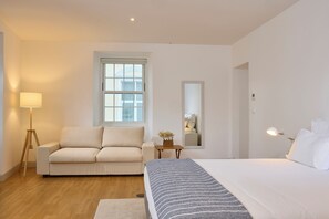 Una habitación de hotel moderna con una cama grande, un sofá, una mesita con una lámpara, una ventana y un espejo.