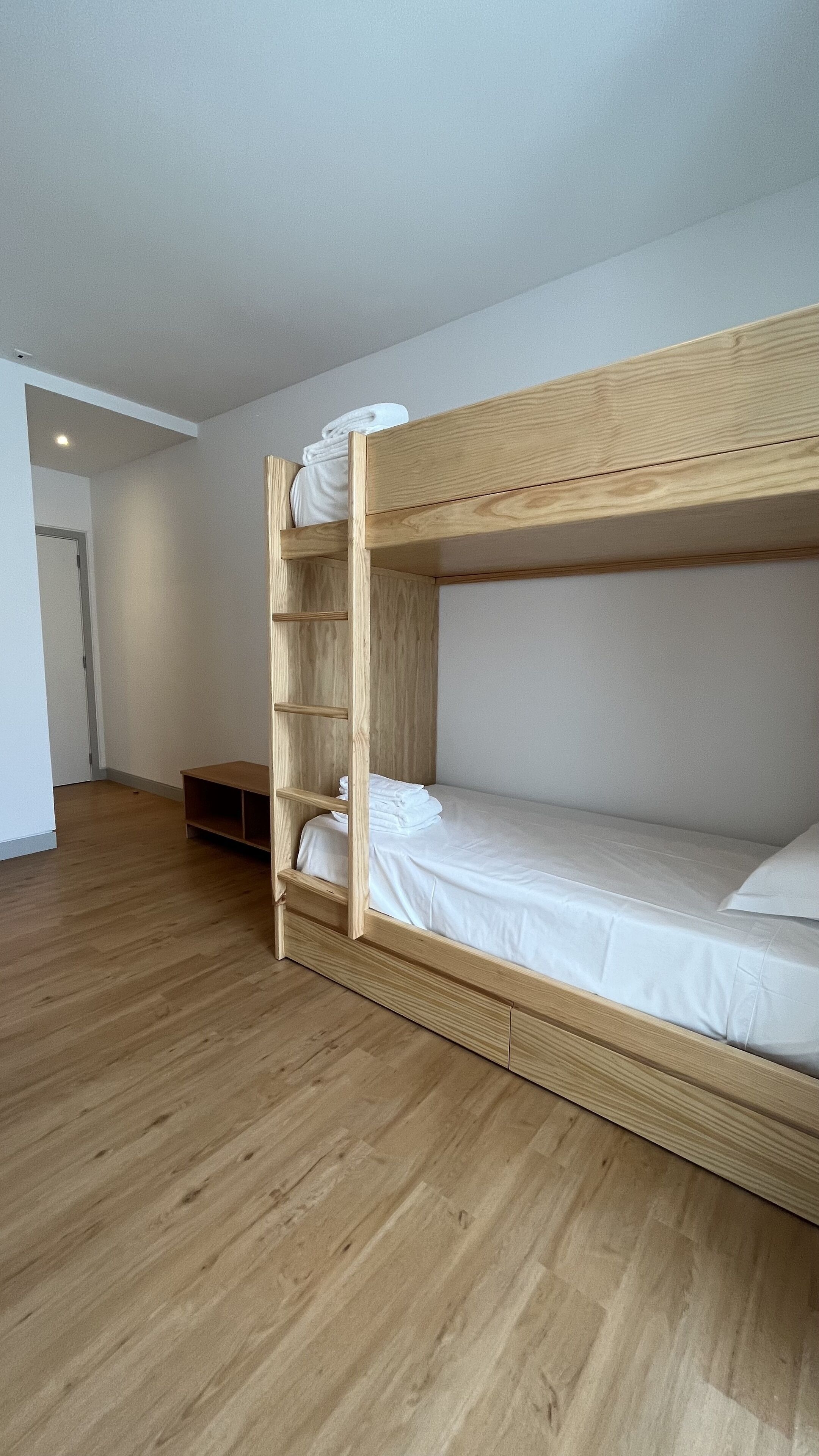 Een stapelbed met houten frame en witte beddengoed, een houten plankenwand en een houten vloer in een kamer met witte muren.
