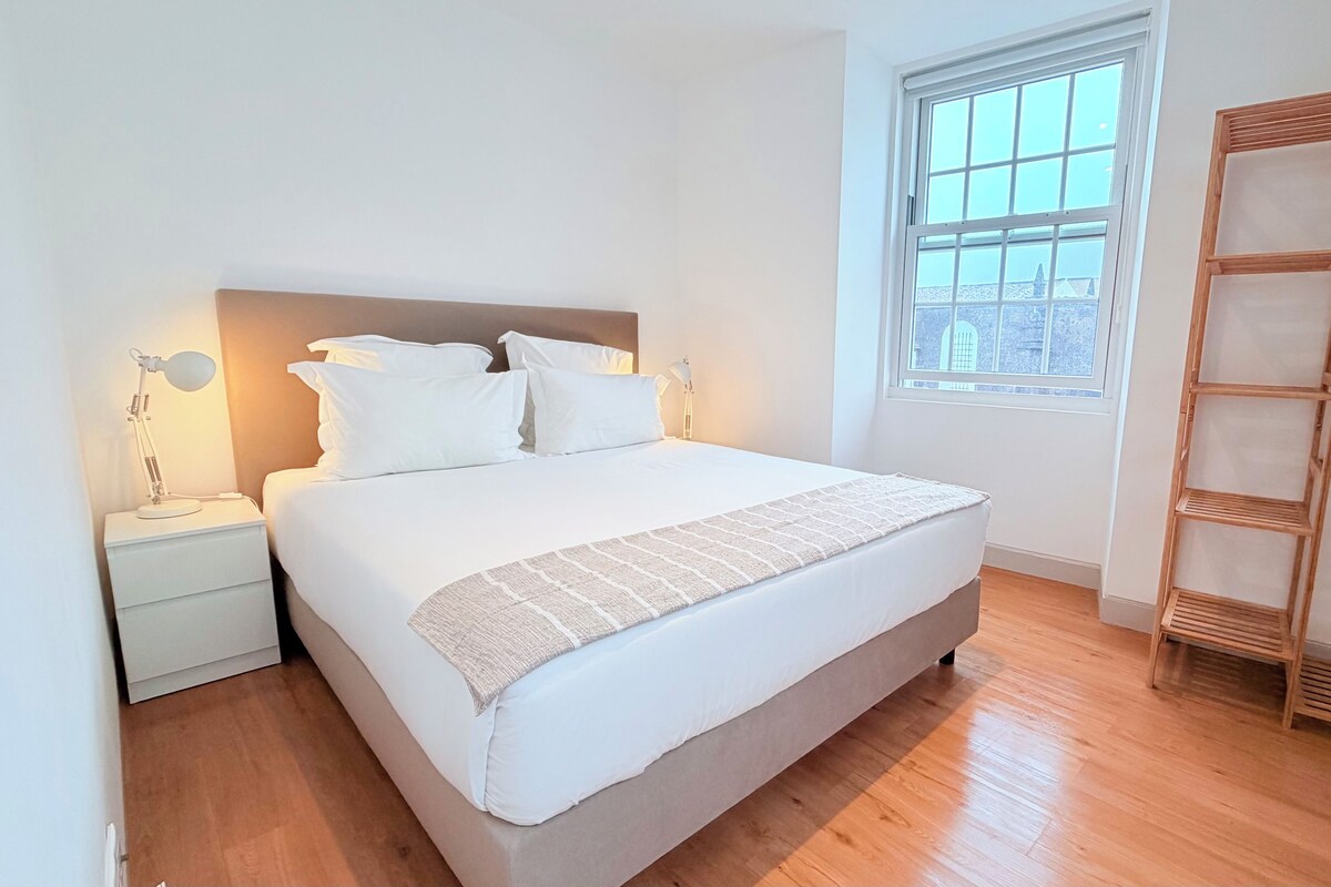 A bedroom with a bed, bedside lamps, a window, and a wooden shelf unit.