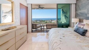 Ein Schlafzimmer mit einem großen Bett, einem Schminktisch, einem Spiegel und einem Balkon mit Blick auf das Meer.