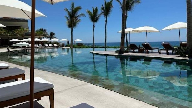 Ein Poolbereich mit Liegestühlen und Sonnenschirmen, Palmen und freiem Blick auf den Ozean.