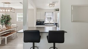 Eine moderne Küche mit weißen Schränken, einer Edelstahl-Kochinsel und einem Essbereich mit Holztisch und schwarzen Barhocker.