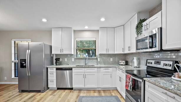 A modern kitchen with white cabinets, stainless steel appliances, and a wooden floor.