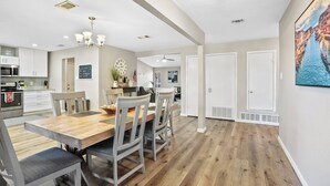 A spacious kitchen with modern appliances, a dining area with a wooden table and chairs, and a hallway leading to a bedroom.