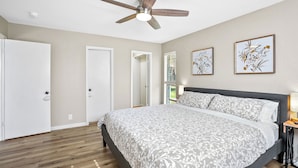 A bedroom with a bed, a ceiling fan, a door, and two framed floral artworks on the wall.